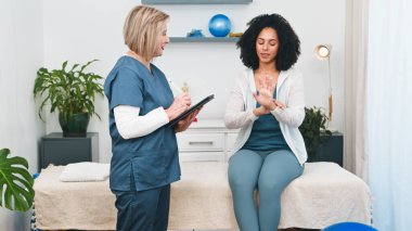 Üst düzey bir fizyoterapist, genç bir siyahi müşterinin profesyonel bir muayene sırasında bilek ağrısı hakkındaki endişelerini dile getirirken özenle kayıt altına alır. Bu özel etkileşim, kişiselleştirilmiş sağlık ve iyileştirme desteğini vurgular