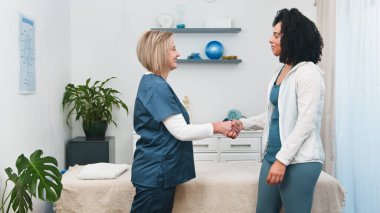 Üst düzey bir fizyoterapist, genç siyahi müşterisini samimi bir şekilde selamlıyor. Kişisel bakım ve güven, spor fizyoterapisi yoluyla iyileşme, sağlık ve sağlığa odaklanmak