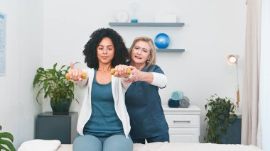 Deneyimli bir kıdemli fizyoterapist, profesyonel küçük muayenehanesinde genç siyahi bir müşteriye özel bakım sağlar. Rehabilitasyon ve iyileşme üzerine odaklanarak, müşteri kolu üzerinde ayrıntılı bir değerlendirme ve hareket yelpazesi uygular.. 