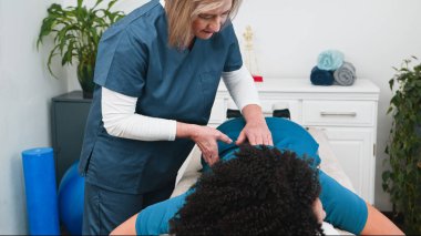 Deneyimli bir kıdemli fizyoterapist genç siyahi müşterilerine özel spor masajı yapıyor. Kas iyileşmesini ve ağrı kesicileri destekliyor.