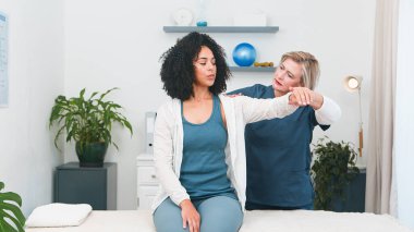 Kendini küçük bir muayenehaneye adamış kıdemli bir fizyoterapist genç bir siyahi müşterinin omzunu ustalıkla tedavi ediyor. Bu profesyonel danışma, kişisel bakımın önemini vurgular. 