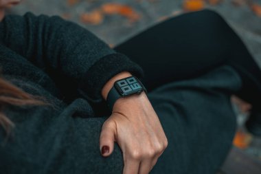 Genç bir kadın bakıyor ve akıllı bir bant kullanıyor. Saat 09: 00 'da. Sonbahar parkındaki kız. Arka plan bulanık. Tam çerçeve