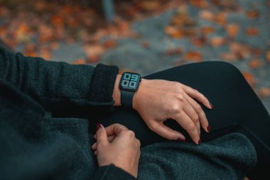 Genç bir kadın bakıyor ve akıllı bir bant kullanıyor. Saat 09: 00 'da. Sonbahar parkındaki kız. Arka plan bulanık. Tam çerçeve