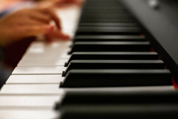 Девушка играет на пианино, крупным планом на фортепиано, белой и черной клавиатуре. Девушка с крупным планом играет мелодию на клавишах электронного синтезатора в гостиной. Высокое качество фото