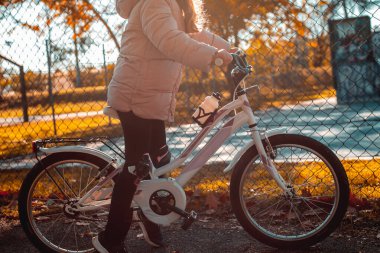 Sarı arka planda bisiklet süren sevimli bir kızın portresi. Sonbahar parkında arka ışıkta bisiklet süren komik çocuk. Yüksek kalite fotoğraf