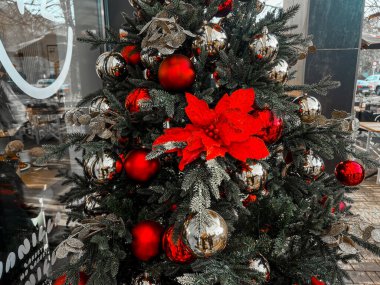 Kırmızı ve gümüş toplarla süslenmiş bir kafe yakınında güzel bir Noel ağacı. İtalya, Milan, San Donato Milano 21.12.2023.