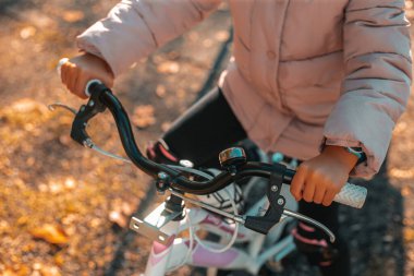 Sarı arka planda bisiklet süren sevimli bir kızın portresi. Sonbahar parkında arka ışıkta bisiklet süren komik çocuk. Kasım ayında sonbahar parkı. Tam çerçeve kenarı. İtalya, Milan. 20.11.2023.