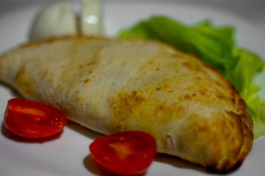 Calzone Doldurulmuş Pizza. Ev yapımı İtalyan eti ve soslu peynirli Calzones. Beyaz tabakta Mozzarella peyniri ve domates. Yüksek kalite fotoğraf