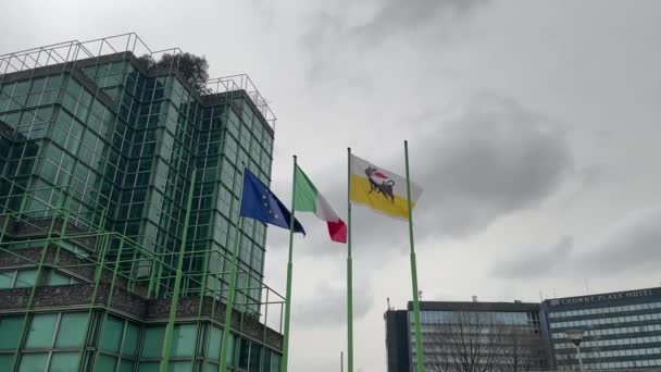 イタリア ミラノ 2024年 イタリアの国旗 ヨーロッパ連合 アジップが オフィスビルの背景と曇りの空と雲に対してゆっくりと動いている — ストック動画