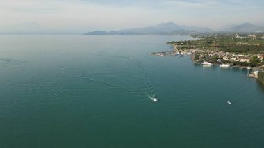 Garda Gölü 'nün güzel panoramik drone manzarası. Güneşli yaz gününde dağlardan ve şehirden oluşan yüksek manzaralı su manzarası. Peschiera del Garda, İtalya. 
