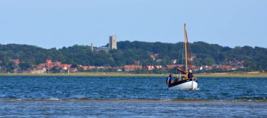 BLAKENEY, NORFOLK, ENGLAND - JULY 13, 2022: Small Fishing Boat at sea with the village of Blakeney Norfolk in Background