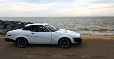 FELIXSTOWE, SUFFOLK, ENGLAND - MAYIS 01, 2022: Arka planda deniz kenarında park etmiş klasik Triumph TR7 arabası.