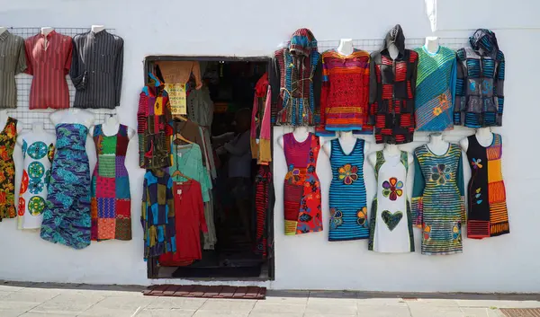 stock image TEGUISE, LANZAROTE, SPAIN - APRIL  23, 2024: Shopfront with colorful garments hanging on wall and doorway