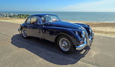 FELIXSTOWE, SUFFOLK, ENGLAND - MAYIS 05, 2024: Klasik Jaguar XK 150 3.8 Coupe arka planda deniz ve deniz kenarına park edilmiş