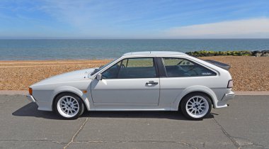 FELIXSTOWE, SUFFOLK, ENGLAND - MAY 05, 2024: Classic VW Scirocco in  White  parked on seafront beach and sea in background clipart