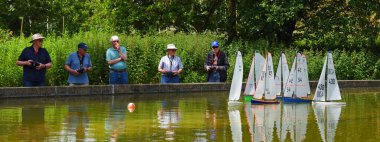 WOODBRIDGE, SUFFOLK, İngiltere - 18 Haziran 2024: Erkekler güneş ışığı altında gölet yatlarında yansımalarla yelken açarlar 