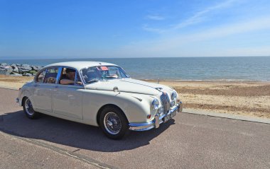 FELIXSTOWE, SUFFOLK, ENGLAND - MAYIS 05, 2024: Arka planda deniz kenarındaki gezinti sahili ve denizde klasik Beyaz Jaguar Mk 2 motorlu arabası