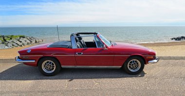 FELIXSTOWE, SUFFOLK, ENGLAND - MAY 05, 2024:  Classic Red Triumph Stag Motor Car Parked on Seafront Promenade. clipart