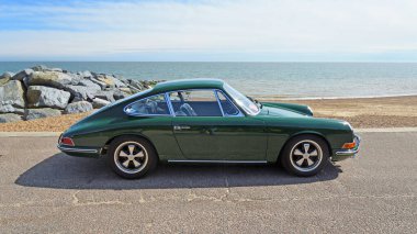 FELIXSTOWE, SUFFOLK, ENGLAND - MAY 05, 2024: Classic Dark Green Porsche 911 S Coupe parked on seafront promenade beach and sea in background  clipart