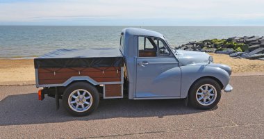 FELIXSTOWE, SUFFOLK, ENGLAND - MAYIS 05, 2024: Arka planda deniz ve deniz manzaralı deniz kenarında park etmiş klasik Morris Minor kamyonet.