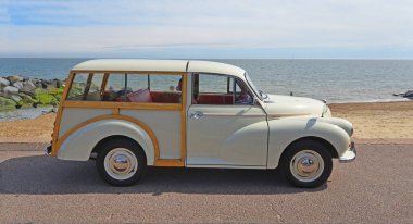 FELIXSTOWE, SUFFOLK, ENGLAND - MAYIS 05, 2024: Klasik Morris Minor Traveller deniz kenarına park etmiş arka plandaki sahil ve deniz kıyısında