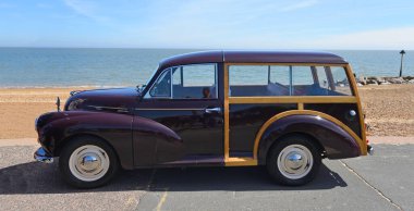 FELIXSTOWE, SUFFOLK, ENGLAND - MAYIS 05, 2024: Arka planda deniz kenarında park etmiş klasik Kızıl Morris Minör Gezgini.