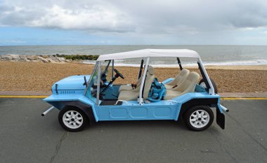 FELIXSTOWE, SUFFOLK, ENGLAND - MAYIS 04, 2025: Arka planda deniz kıyısındaki klasik açık mavi Mini Moke Parkı