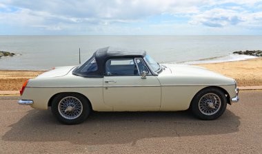 FELIXSTOWE, SUFFOLK, ENGLAND - MAYIS 04, 2025: Arka planda deniz kenarında park etmiş klasik Beyaz MGB Roadster