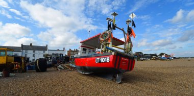 ALDEBURGH, SUFFOLK, İngiltere - 24 Eylül 2024: Arka plandaki Aldeburgh sahil binalarında kırmızı balıkçı teknesi.