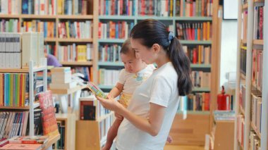 Genç anne bir kitapçıda bebeğe renkli bir kitap gösteriyor. Yüksek kalite 4k görüntü