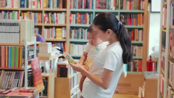 Jonge Moeder Toont Een Gekleurd Boek Aan Baby Een Boekenwinkel — Stockvideo