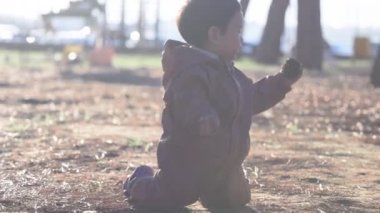 Sevimli erkek bebek yerde oturur ve gün batımının önünde sopalarla oynar. Yüksek kalite 4k görüntü