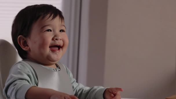 Ένα Χαρούμενο Μωρό Χαμογελάει Στην Καρέκλα Και Τρώει Από Κουτάλι — Αρχείο Βίντεο