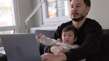 Dizüstü bilgisayarda çalışan genç bir adam oğlunu evde tutuyor. Uzaktan kumanda. Yüksek kalite 4k görüntü