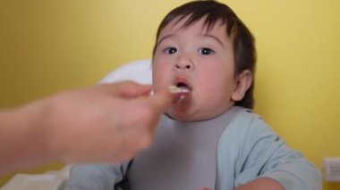 Anne bebeğini kaşıkla besliyor. Tamamlayıcı gıdaların tanıtımı, iyi beslenme, bebek maması yüksek kalite 4K görüntü