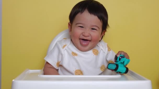 可愛いアジア系の赤ちゃんがおもちゃを持って上に座り 黄色い背景で笑っています 高品質4K映像 — ストック動画