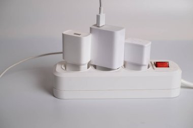 Birçok şarj aleti beyaz arka plandaki bir elektrik prizine bağlıdır..