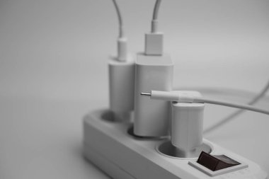 Birçok şarj aleti beyaz arka plandaki bir elektrik prizine bağlıdır..