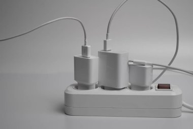 Birçok şarj aleti beyaz arka plandaki bir elektrik prizine bağlıdır..