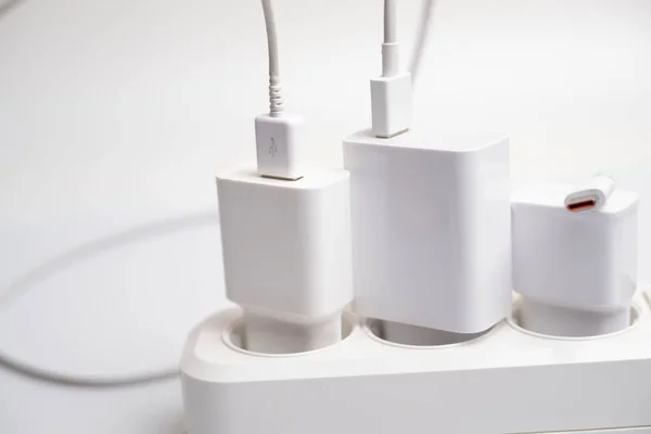 Birçok şarj aleti beyaz arka plandaki bir elektrik prizine bağlıdır..