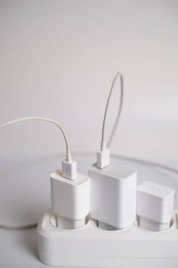 Birçok şarj aleti beyaz arka plandaki bir elektrik prizine bağlıdır..