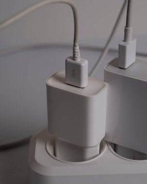 Birçok şarj aleti beyaz arka plandaki bir elektrik prizine bağlıdır..