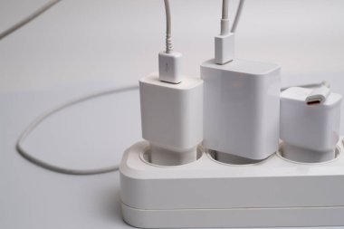 Birçok şarj aleti beyaz arka plandaki bir elektrik prizine bağlıdır..