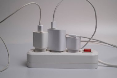 Birçok şarj aleti beyaz arka plandaki bir elektrik prizine bağlıdır..