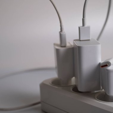 Birçok şarj aleti beyaz arka plandaki bir elektrik prizine bağlıdır..
