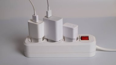 Birçok şarj aleti beyaz arka plandaki bir elektrik prizine bağlıdır..
