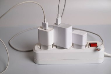 Birçok şarj aleti beyaz arka plandaki bir elektrik prizine bağlıdır..