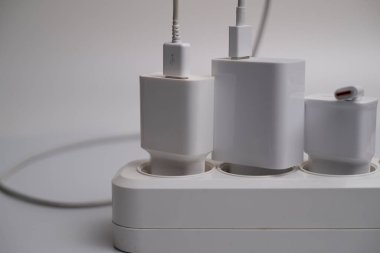 Birçok şarj aleti beyaz arka plandaki bir elektrik prizine bağlıdır..