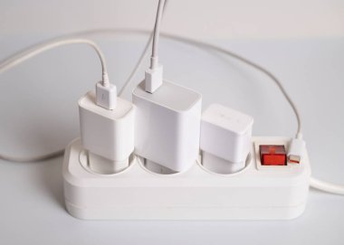 Birçok şarj aleti beyaz arka plandaki bir elektrik prizine bağlıdır..