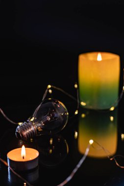 Ampuller ve yanan bir mum siyah bir arka planda. Aynı zamanda çelenk, bokeh. bayram karartması konsepti
